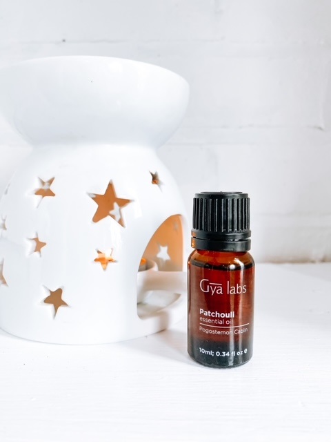 A small bottle of patchouli essential oil on a white shelf, next to an essential oil burner, showing patchouli diffuser blends
