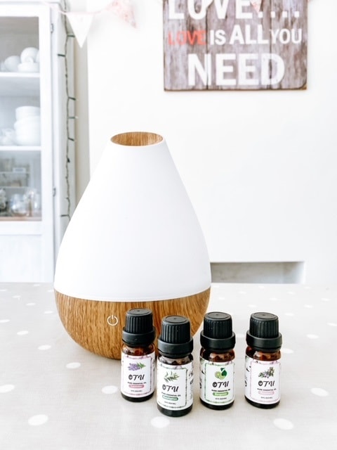 A diffuser on a table with essential oil bottles in front.